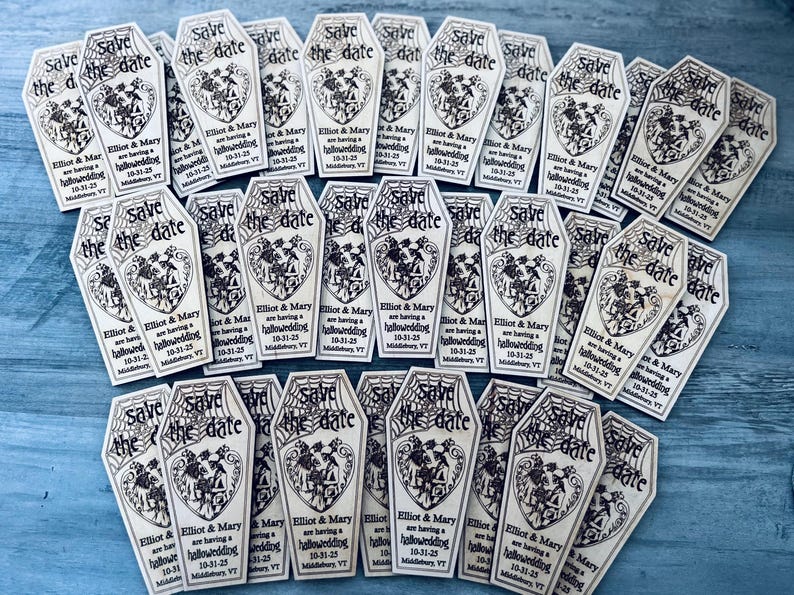May include: A collection of save the date cards shaped like coffins with a spiderweb design and the text "Save the date" and "Elliot & Mary are having a hallowedding 10-31-25 Middlebury, VT".