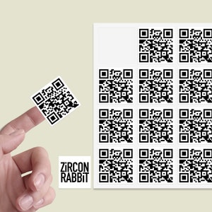 Könnte beinhalten: Ein Blatt mit weißen Aufklebern mit schwarzen QR-Codes. Es gibt insgesamt 12 QR-Codes, die in einem 3x4-Raster angeordnet sind. Die Aufkleber befinden sich auf einem hellbeigen Hintergrund. Der Text "ZIRCON RABBIT" ist auf einem der Aufkleber gedruckt.