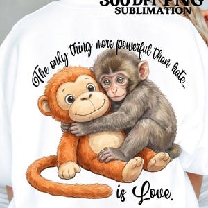 Könnte beinhalten: Weißes Sweatshirt mit einer Grafik von zwei sich umarmenden Affen. Einer ist orange und lächelt, der andere ist grau. Der Text lautet: „Das Einzige, was mächtiger ist als Hass... ist Liebe.“
