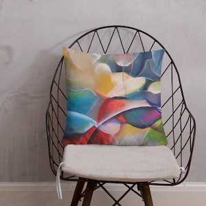 May include: A colorful abstract pillow with shades of blue, green, yellow, red, and purple. The pillow is sitting on a black wire chair with a white cushion.