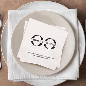 Może przedstawiać: Formalne nakrycie stołu z białą serwetką i dwoma talerzami. Na talerzu znajduje się biała serwetka z czarnym logo i tekstem. Widoczne są również sztućce i kieliszek do wina. Tekst na serwetce brzmi "YOUR LOGO HERE" i "COMPANY TAGLINE SLOGAN INFORMATION WWW.YOURWEBSITE.COM".