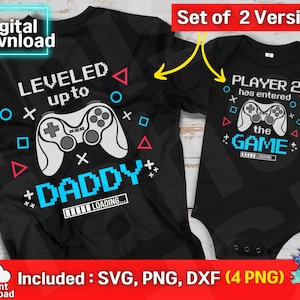 May include: Two black t-shirts with a gamer theme. One shirt says "LEVELED up to DADDY" with a video game controller graphic. The other shirt says "PLAYER 2 has entered the GAME".