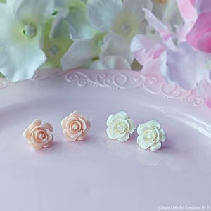 May include: Four delicate rose-shaped earrings in two colors: pink and white. The earrings are displayed on a pink plate.