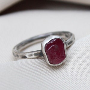 May include: A silver ring with a hammered band and a red gemstone set in the center.