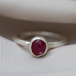 Peut inclure: Une bague en argent avec une pierre ovale rouge foncé sertie au centre.