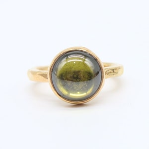May include: A gold ring with a round, dark green gemstone.