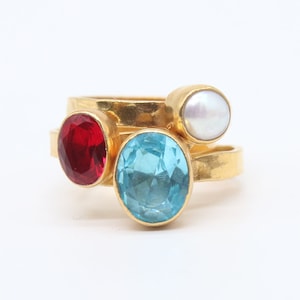 May include: Gold ring with three stones: a red stone, a blue stone, and a white pearl.