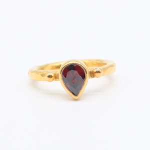 May include: A gold ring with a teardrop-shaped red gemstone.