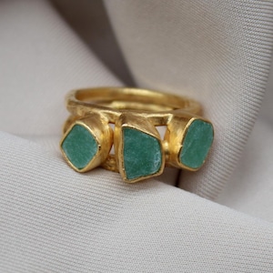May include: Gold ring with three green gemstone accents.