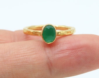 May include: A gold ring with a green oval gemstone. The ring is on a finger.