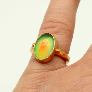 May include: A gold ring with a large oval-shaped iridescent gemstone. The gemstone is green, yellow, and orange.