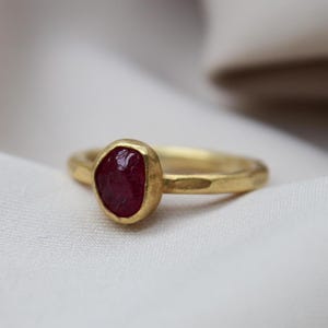 Puede incluir: Un anillo de oro con una piedra preciosa de rubí rojo. El anillo tiene una textura martillada y el rubí está engastado en un engaste de bisel.