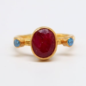 Peut inclure: Une bague en or avec une grande pierre de rubis ovale et deux petites pierres bleues de chaque côté.