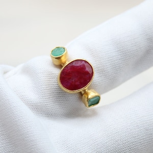 May include: A gold ring with a red oval gemstone and two smaller green oval gemstones.