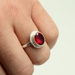 May include: A silver ring with a red oval gemstone set in a bezel setting.