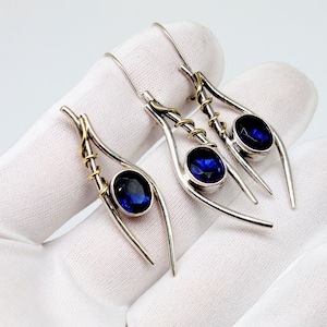 May include: A pair of silver earrings with blue gemstones and gold accents. The earrings are shaped like a teardrop and have a delicate, intricate design.
