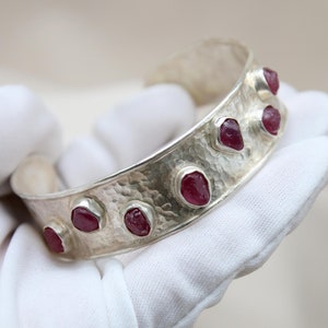 May include: A silver bracelet with a hammered finish and set with eight red gemstones.