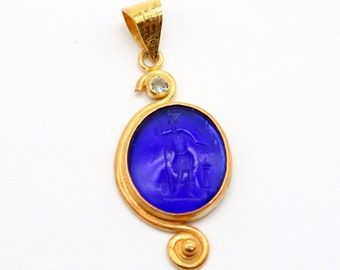 May include: A gold pendant with a blue glass cameo featuring a carved figure. The pendant has a swirl design and a small clear stone.