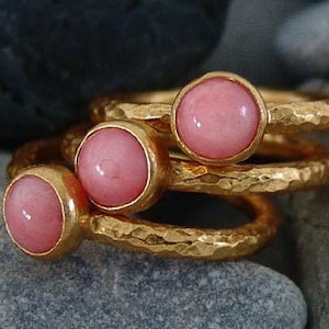 May include: Three gold rings with pink gemstones. The rings are stacked on top of each other and have a hammered texture.