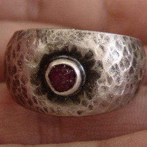 May include: A silver ring with a hammered texture and a red gemstone set in the centre.
