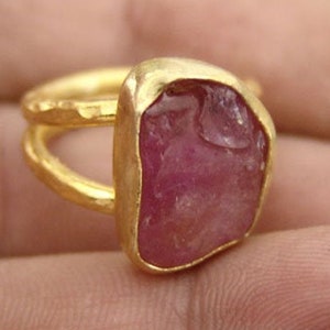Pode incluir: Um anel de ouro com uma grande gema rosa bruta. O anel &eacute; usado em um dedo.