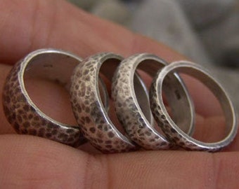 May include: Four silver rings with a textured hammered finish. The rings are stacked on top of each other.
