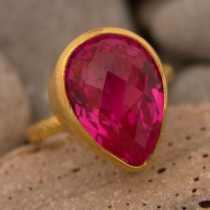 Pode incluir: Um anel de ouro com uma gema rosa em forma de lágrima.