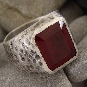 May include: A silver ring with a textured band and a large, dark red gemstone.