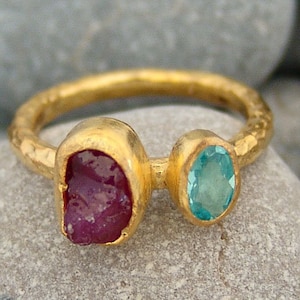 Op de afbeelding: Een gouden ring met een rode en blauwe edelsteen bezetting. De ring is getextureerd en heeft een gehamerde afwerking.