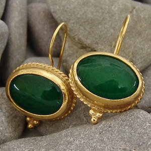 May include: A pair of gold earrings with green oval-shaped gemstones. The earrings have a delicate, ornate design.
