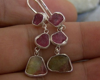 May include: Silver earrings with pink and green gemstone drops. The earrings feature three teardrop-shaped gemstones on each earring.