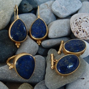 May include: A set of gold earrings and cufflinks with dark blue gemstone accents. The earrings are teardrop shaped and the cufflinks are oval.