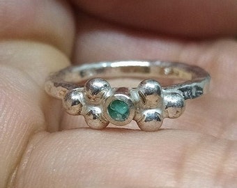 May include: A silver ring featuring a cluster of small round beads with a single green gemstone at the centre.
