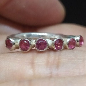 May include: A silver ring with seven pink gemstones set in a row.