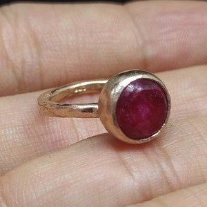 Może przedstawiać: Pierścionek z głębokim czerwonym kamieniem szlachetnym osadzonym w młotkowanej złotej obrączce.