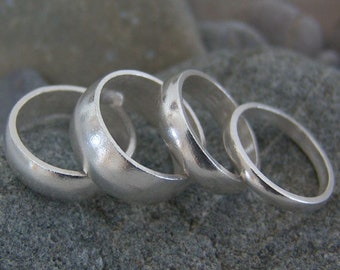 May include: Four silver rings of varying sizes stacked on top of each other. The rings are smooth and have a rounded shape.