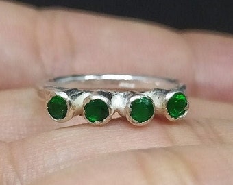 May include: A silver ring with four green gemstones set in a row.