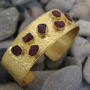 May include: Gold cuff bracelet with a hammered texture and six red gemstones set into the metal.