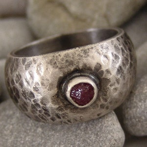 May include: A silver ring with a hammered texture and a single red gemstone set in the centre.