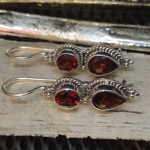 Op de afbeelding: Een paar zilveren oorbellen met rode edelsteen druppels. De oorbellen hebben een delicaat, ingewikkeld ontwerp en zijn perfect om elke outfit een vleugje elegantie te geven.