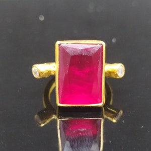 Peut inclure: Une bague en or avec une grande pierre précieuse rectangulaire rouge foncé et deux petites pierres rondes blanches sur la bande.