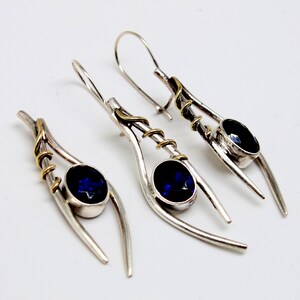 May include: A pair of silver earrings with blue gemstones and gold accents. The earrings are designed with a curved, abstract shape.