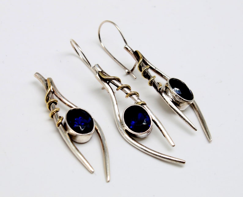 May include: A pair of silver earrings with blue gemstones and gold accents. The earrings are designed with a curved, abstract shape.