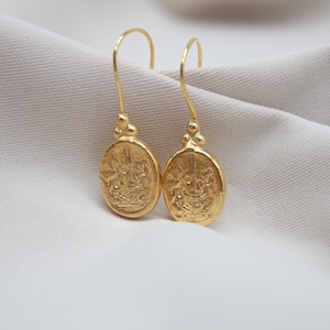 May include: A pair of gold-toned dangle earrings with a detailed oval design. The earrings feature a textured surface and a delicate drop.