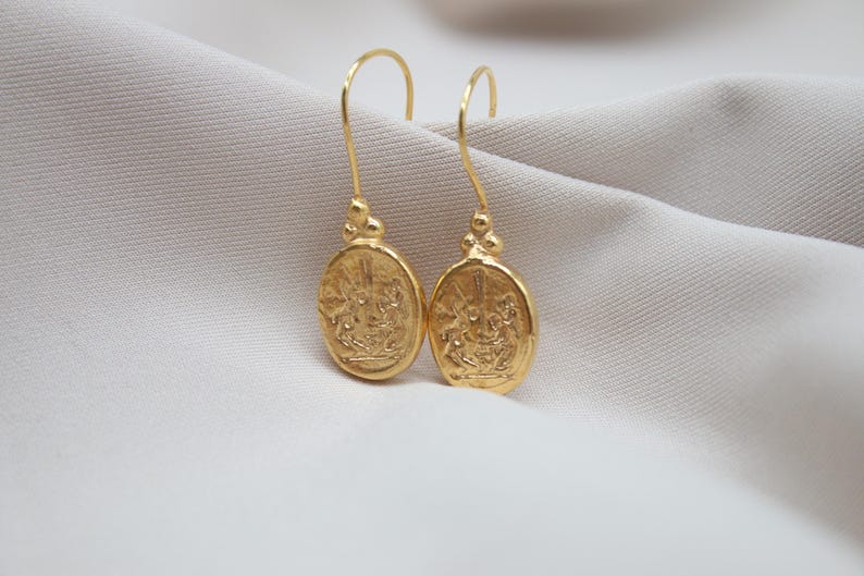 May include: A pair of gold-toned dangle earrings with a detailed oval design. The earrings feature a textured surface and a delicate drop.