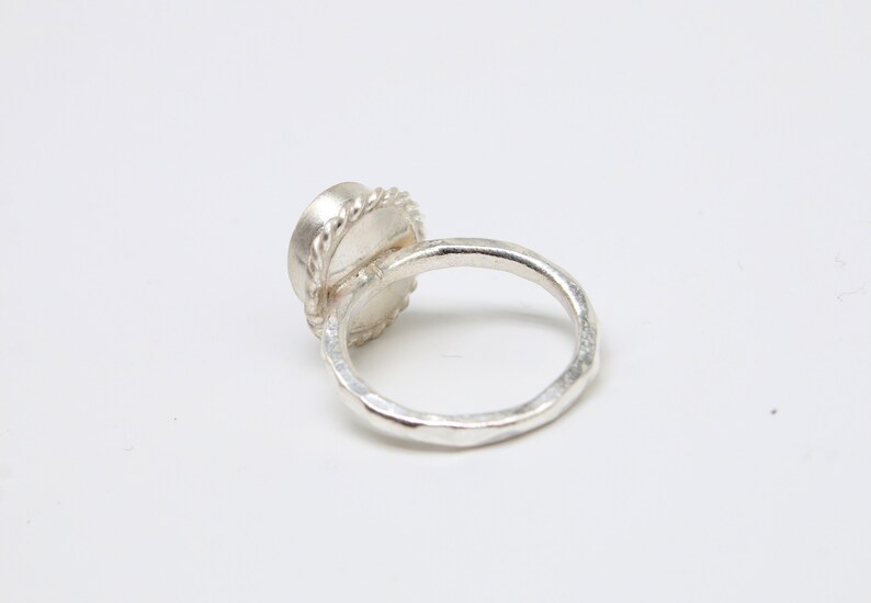 Op de afbeelding: Een zilveren ring met een getextureerde band en een ronde, bezel-gezet edelsteen.