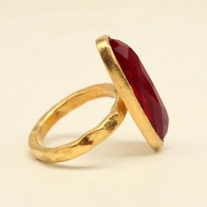 May include: A gold ring with a large, faceted, red gemstone. The ring band is textured and has a hammered finish.
