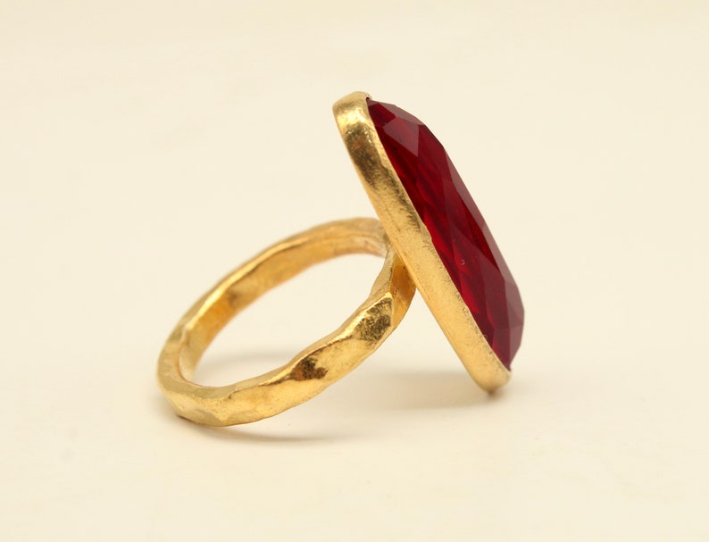 May include: A gold ring with a large, faceted, red gemstone. The ring band is textured and has a hammered finish.