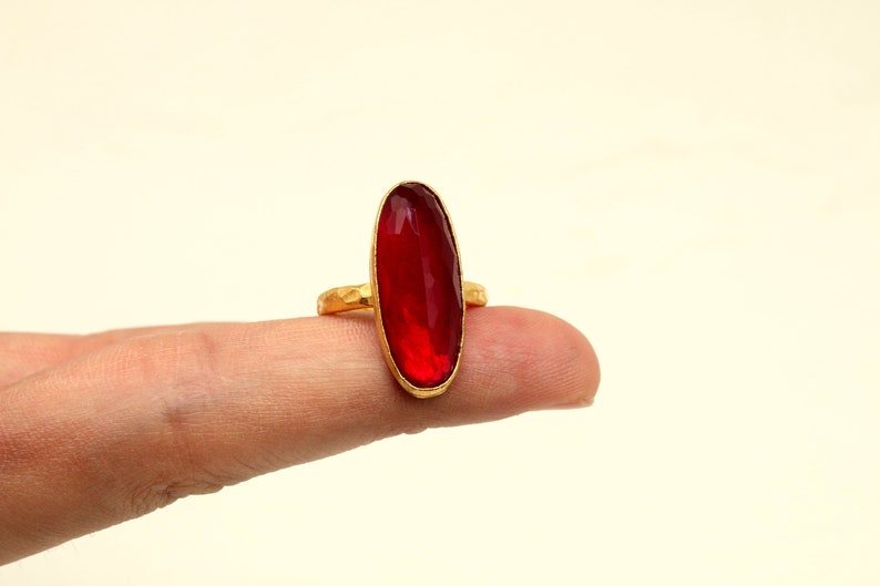 Może przedstawiać: Złoty pierścionek z dużym, owalnym, czerwonym kamieniem szlachetnym.