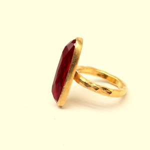 May include: A gold ring with a large, red, faceted gemstone. The band of the ring is textured.